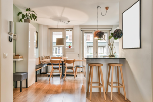 Comedor con barra de desayuno, sillas de madera y gran entrada de luz natural, ejemplo de distribución funcional en reformas de pisos pequeños.