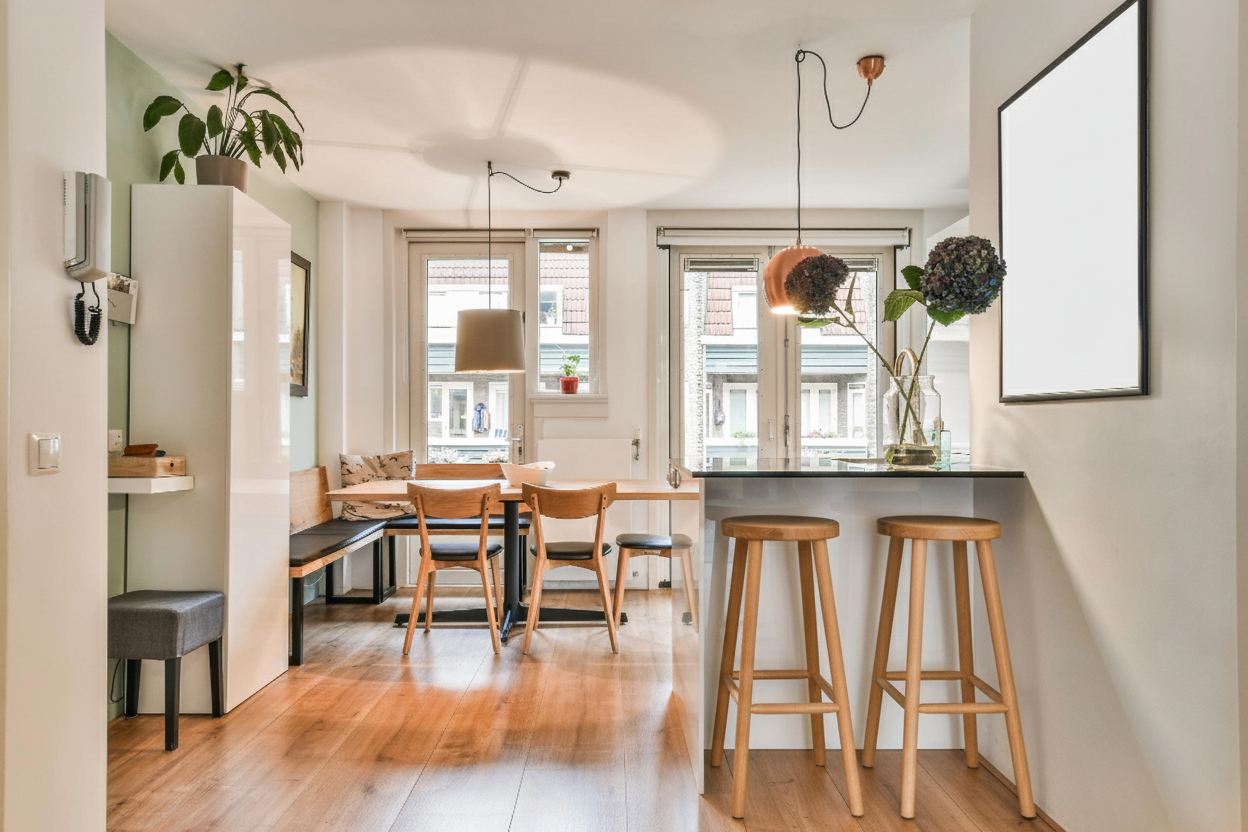 Comedor con barra de desayuno, sillas de madera y gran entrada de luz natural, ejemplo de distribución funcional en reformas de pisos pequeños.